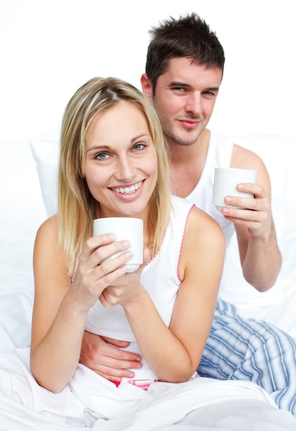 Couple, boire du café dans le lit et souriant à la caméra