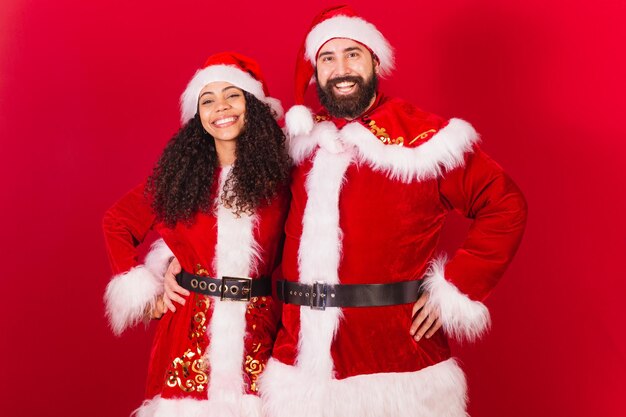 Photo couple brésilien habillé pour noël père noël maman noël femme noire et homme caucasien souriant à la caméra