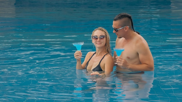 Couple câlins et bisous buvant de l'alcool cocktail bleu dans la piscine de l'hôtel en plein air