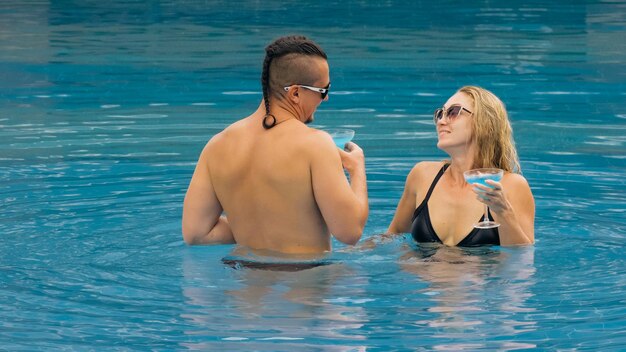 Couple câlins et bisous buvant de l'alcool cocktail bleu dans la piscine de l'hôtel en plein air