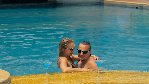 Couple câlins et bisous buvant de l'alcool cocktail bleu dans la piscine de l'hôtel en plein air