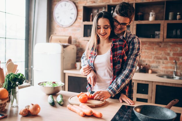 Couple câlins lors de la cuisson de la salade de légumes frais dans un bol sur la cuisine.