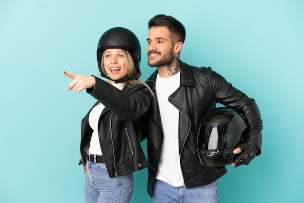 Couple avec casque de moto sur fond bleu isolé pointant vers le côté pour présenter un produit