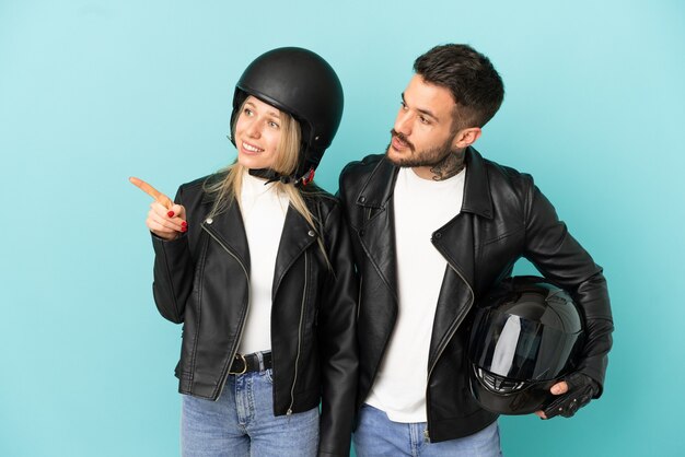 Couple avec casque de moto sur fond bleu isolé présentant une idée tout en souriant vers