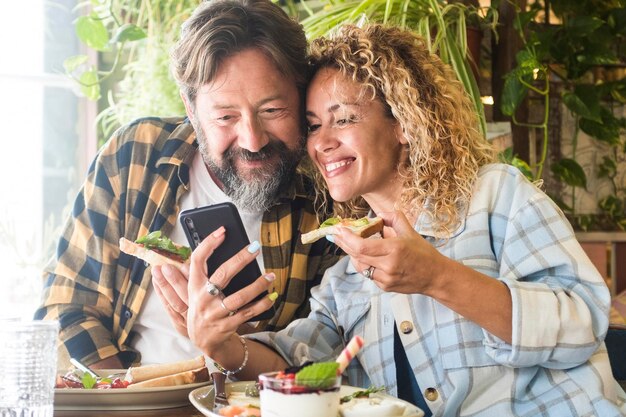 Couple caucasien adulte homme et femme en vidéoconférence appel sur téléphone portable pendant le déjeuner dans un restaurant de café ensemble des hipsters heureux et joyeux utilisent une connexion Wi-Fi sans fil à Internet