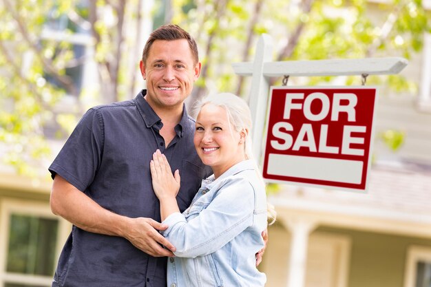 Un couple caucasien devant un panneau immobilier et une maison à vendre