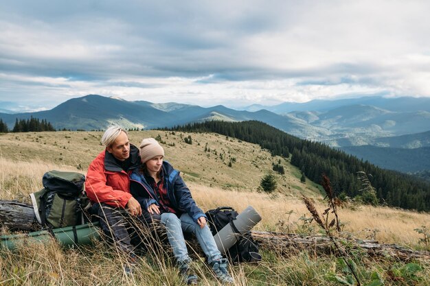 Photo couple caucasien homme et femme sont assis sur un arbre tombé paysage d'été naturel touristes voyageant à travers les montagnes amis à l'arrêt pendant un voyage dans les montagnes copier l'espace