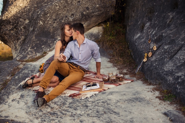 Couple charmant sensuel dans des câlins chauds sur des vêtements décontractés assis sur le plaid sur le rocher avec une décoration d'automne.