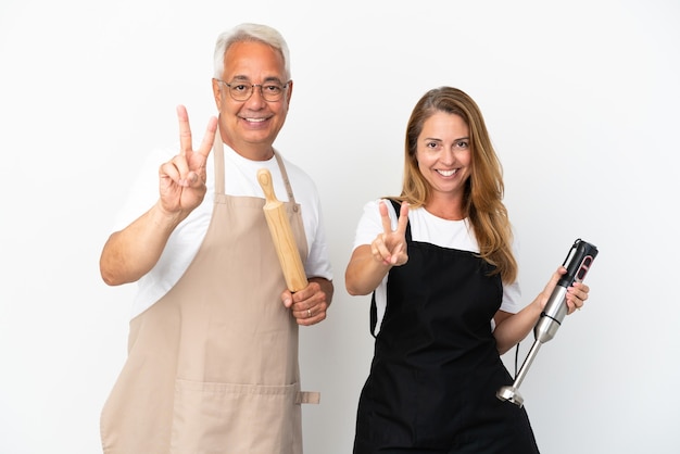 Couple de chefs d'âge moyen isolé sur fond blanc souriant et montrant le signe de la victoire