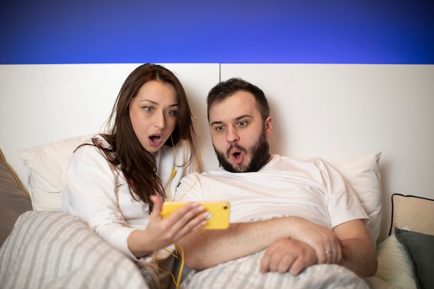 Couple choqué et effrayé à regarder des films d'horreur sur smartphone couché dans son lit