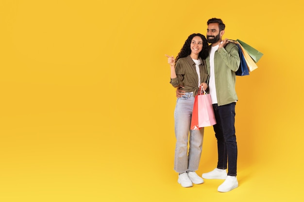 Couple de clients du Moyen-Orient avec des sacs pointant de côté fond jaune