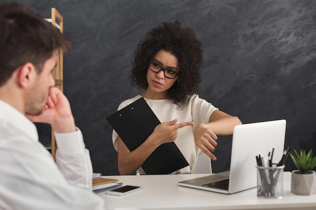 Couple concentré de jeunes collègues travaillant dans un bureau moderne. Femme noire sérieuse hr interviewant un candidat masculin, parlant de ponctualité, espace de copie