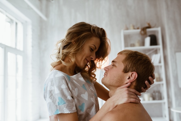 Couple dans la chambre sur le lit. Une fille blonde en pyjama, un gars avec un torse nu. Période de Noël. Une couverture de grand accouplement.