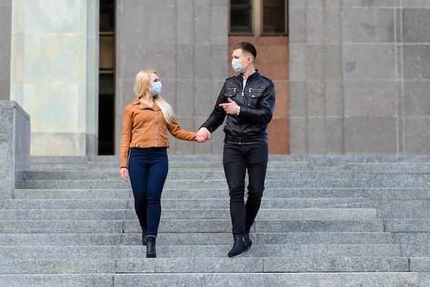 Couple dans des masques de protection se promener à l'extérieur dans la ville près du bâtiment commercial au moment de la quarantaine. Conception du coronavirus.