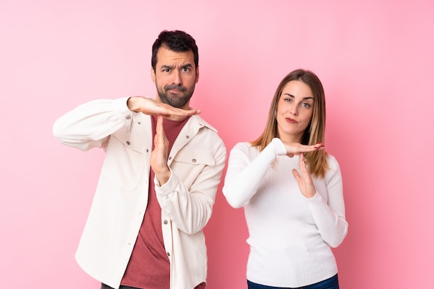 Couple dans la Saint-Valentin sur un mur rose isolé faisant un geste d'arrêt avec sa main pour arrêter un acte