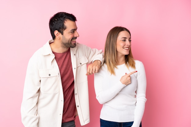 Photo couple dans la saint-valentin sur un mur rose isolé pointant vers le côté pour présenter un produit