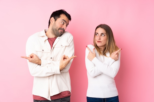 Couple dans la Saint-Valentin sur mur rose isolé pointant vers les latéraux ayant des doutes