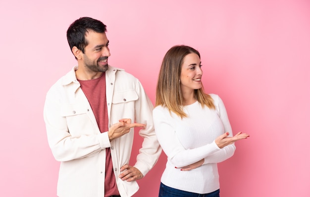 Couple dans la Saint-Valentin sur un mur rose isolé, tendant les mains sur le côté pour inviter à venir