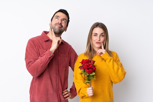 Couple dans la Saint-Valentin tenant des fleurs sur un mur isolé en pensant à une idée tout en