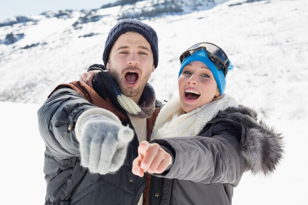 Couple dans les vestes pointant sur la caméra sur le paysage couvert de neige