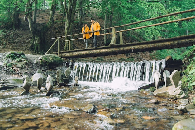 Couple debout au pont en bois traverser la rivière des montagnes