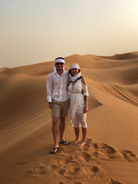 Photo un couple debout sur une dune de sable dans le désert.