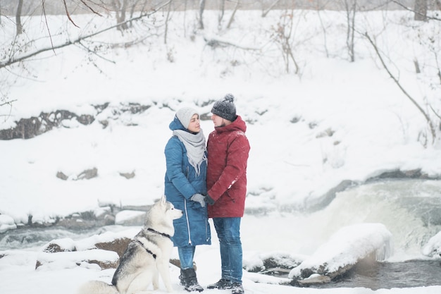 Couple debout avec husky sibérien dans la neige en hiver. cascade. Saint Valentin. Chute de neige. Famille heureuse. Chien. se tenant la main. Photo de haute qualité