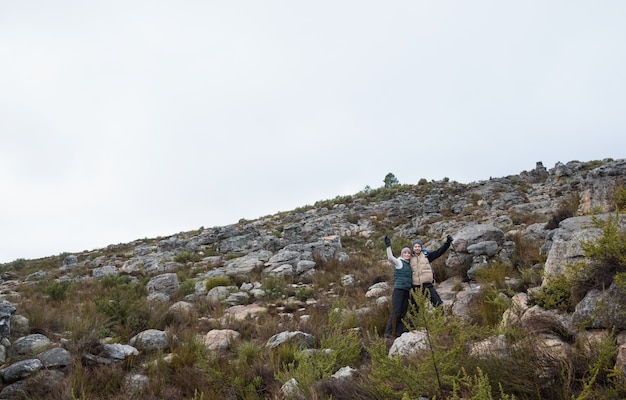 Couple debout sur un paysage rocheux avec les mains levées contre le ciel clair