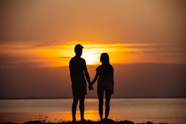 Le couple debout près d'une eau sur le fond du lever du soleil