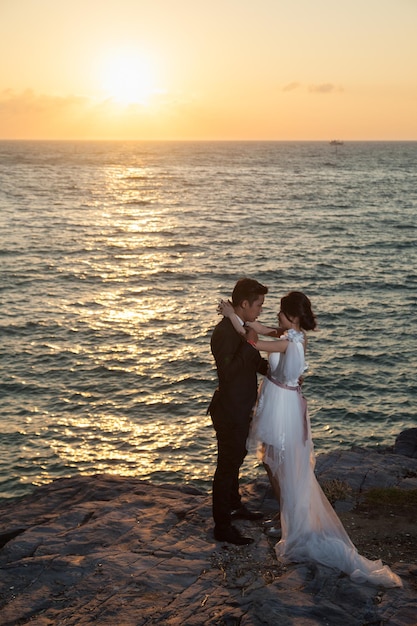 Un couple debout sur des rochers au bord de la mer au coucher du soleil