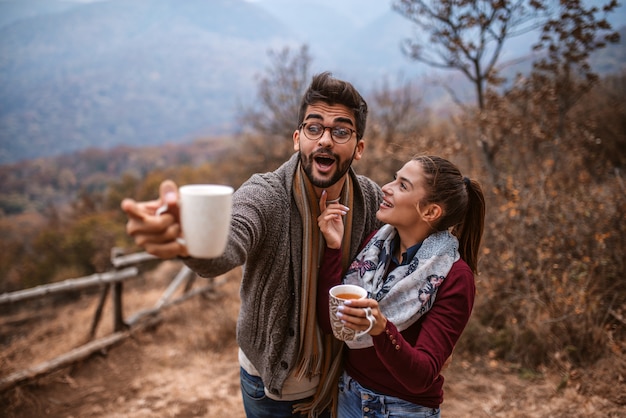 Couple debout avec des tasses dans les mains. Homme montrant quelque chose.