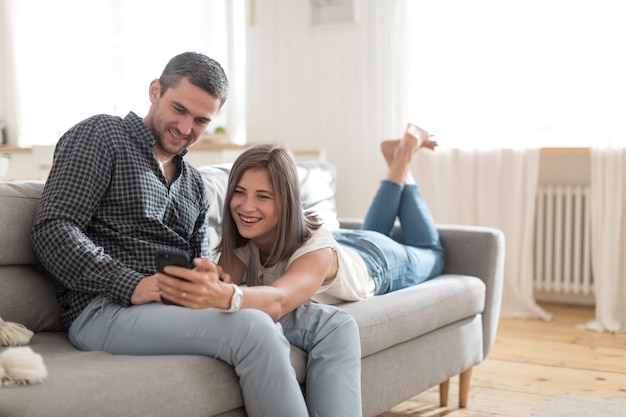 Couple décontracté positif prenant une photo sur un smartphone tout en se reposant sur un canapé à la maison