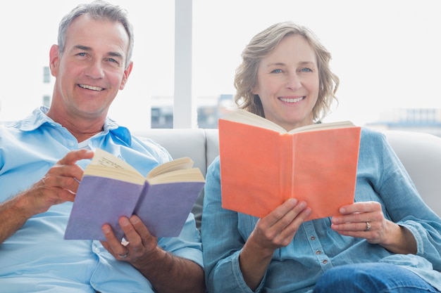 Couple détendue, lire des livres sur le canapé en souriant à la caméra