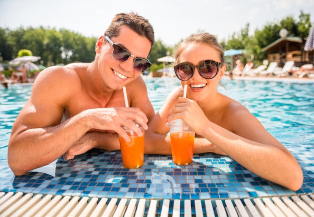Couple de détente dans la piscine de la station, en buvant des cocktails.