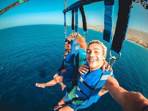 Couple de deux personnes heureuses profitant de l'été et des vacances en faisant des activités extrêmes sur la mer avec un bateau - de belles personnes prenant un selfie tout en faisant du parachute ascensionnel ensemble