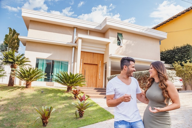 Couple devant la nouvelle grande maison moderne, à l'extérieur, tenant la clé. Couple heureux avec maison de rêve en arrière-plan.