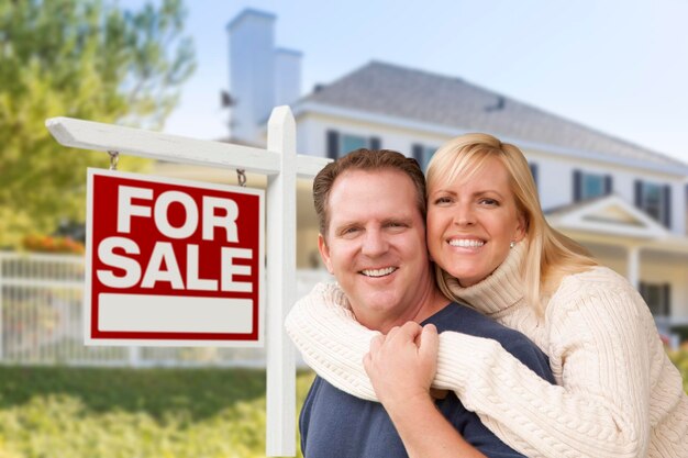 Un couple devant une nouvelle maison et un panneau immobilier