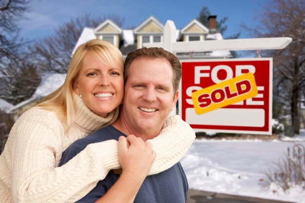 Un couple devant une nouvelle maison et un panneau immobilier