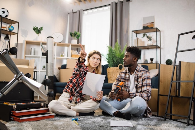 Couple diversifié conseillant sur le placement de meubles dans un appartement