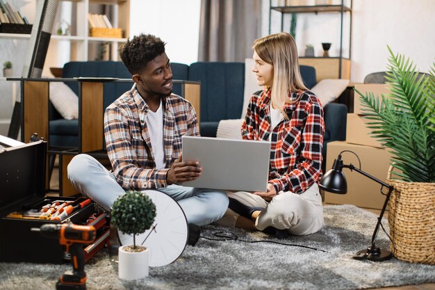 Couple diversifié dans un nouvel appartement à l'aide d'un ordinateur portable