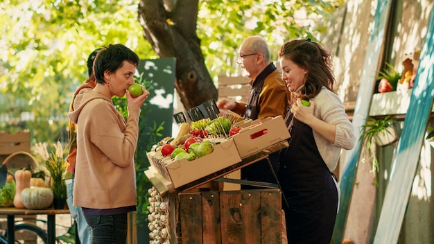 Couple diversifié visitant le comptoir du marché des agriculteurs avec des vendeurs, cherchant à acheter des produits bio frais de la foire de rue. Homme et femme achetant des légumes biologiques au marché vert.