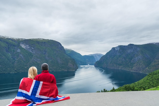 Le couple avec le drapeau de la Norvège regarde le fjord