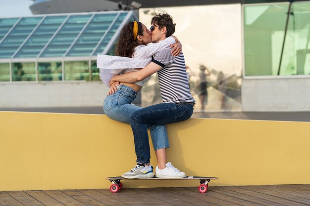 Couple élégant s'embrassant assis dans le skatepark jeunes longboarders mignons homme et femme amoureux câlins