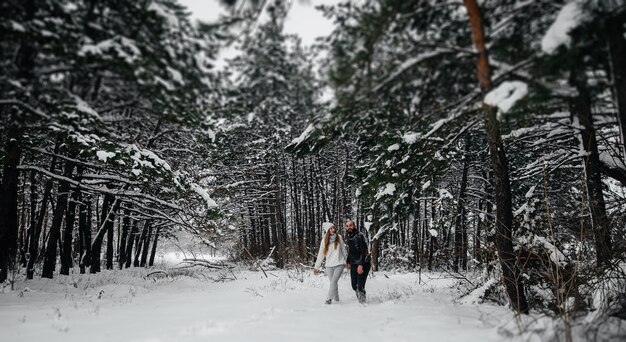 Un couple embrasse dans une forêt enneigée sur un fond d'arbres