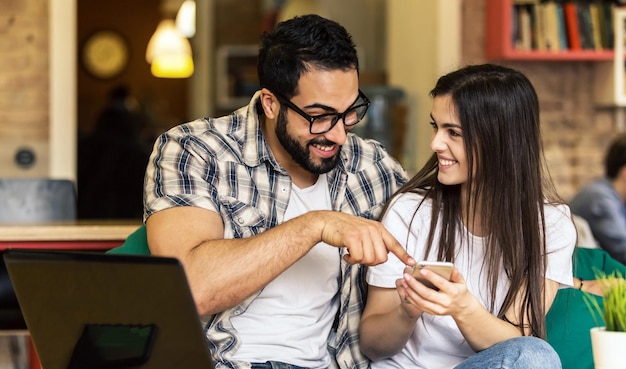 Couple d'employés de bureau barbu à lunettes et fille brune s'amusant à regarder des photos prises sur smartphone