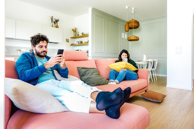 Photo couple ennuyé dans un moment de désintérêt s'ignorant à l'aide d'un téléphone portable à la maison concept d'apathie tristesse avec homme et femme accro aux nouvelles technologies filtre lumineux