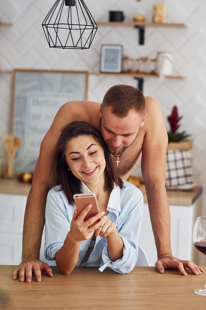 Couple ensemble dans la cuisine le matin avec un téléphone portable.