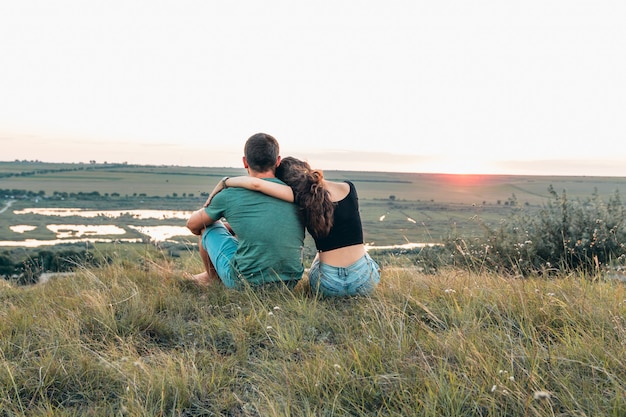 Couple est étreignant et assis près d'une colline au coucher du soleil