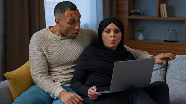 Couple ethnique marié mari femme homme afro-américain utiliser un ordinateur portable avec une femme musulmane arabe dans