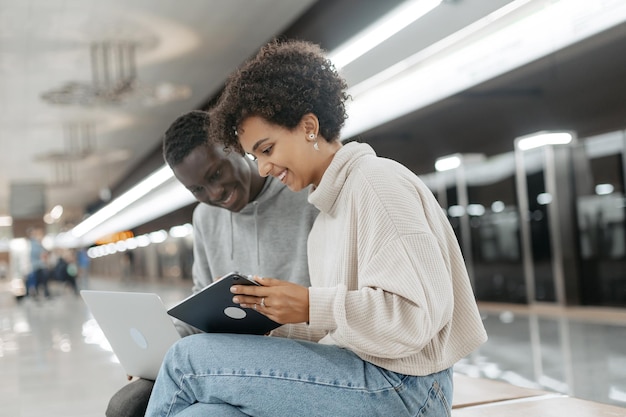 Couple d'étudiants avec des appareils en attente d'une rame de métro